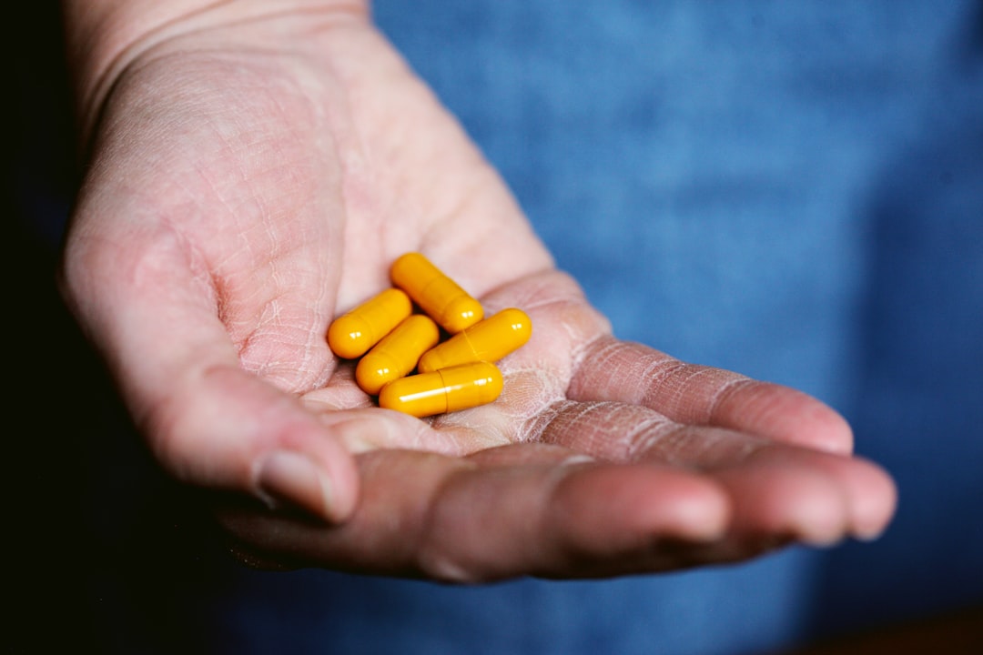 Orange pills. by Vitamin Brands yellow medication pill on persons hand